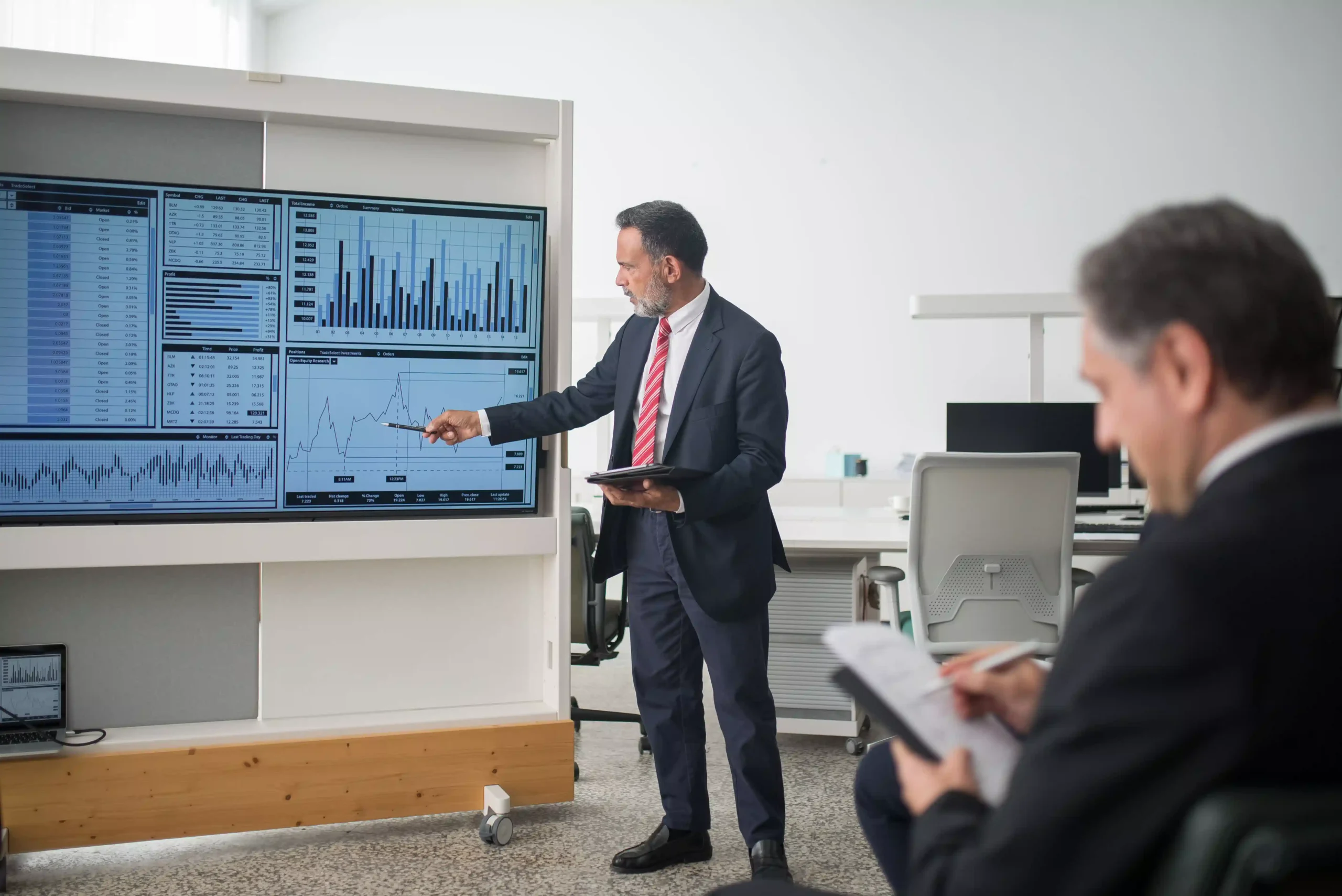 Un ejecutivo señala gráficos de inversión en una pantalla durante una reunión en una oficina