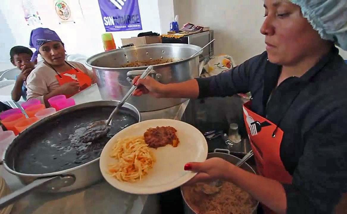 Mujeres cocinando y sirviendo platos de comida en un comedor comunitario