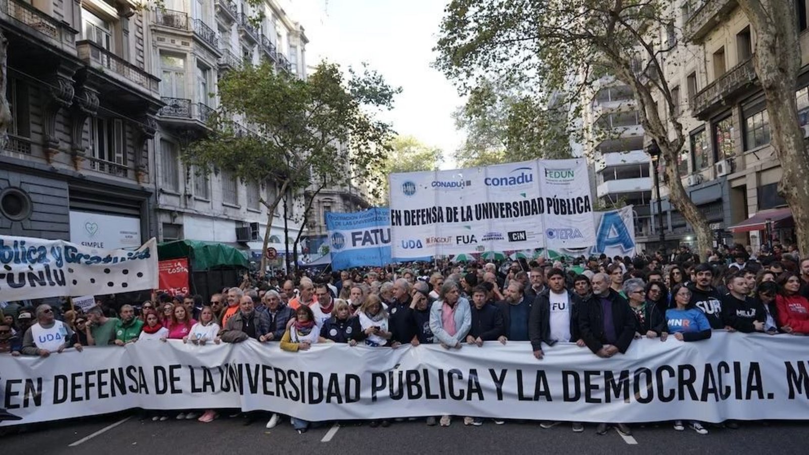 Columna de la Marcha Federal Universitaria con banderas de gremios docentes y una bandera que dice En defensa de la universidad pública y la democracia
