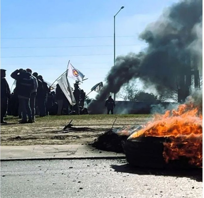 Trabajadores con banderas sindicales junto a una columna de humo y un neumático encendido en el acceso al parque industrial de Gualeguaychú